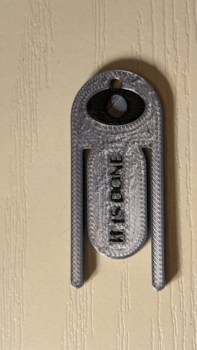 The &lsquo;It Is Done&rsquo; clip, 3-D printed in silver and black — the waking eye, the crystal seat, and the decree, held against the light