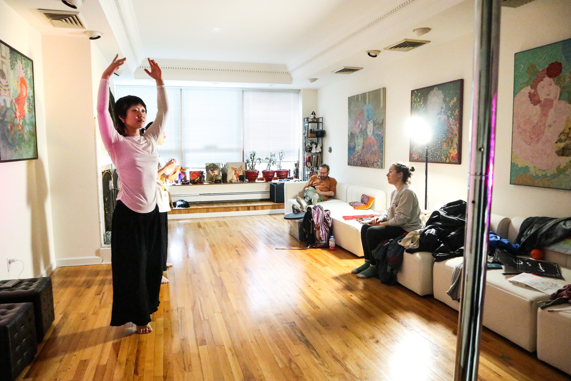 An artist in residence moving through the full studio space — arms raised, artwork on the walls