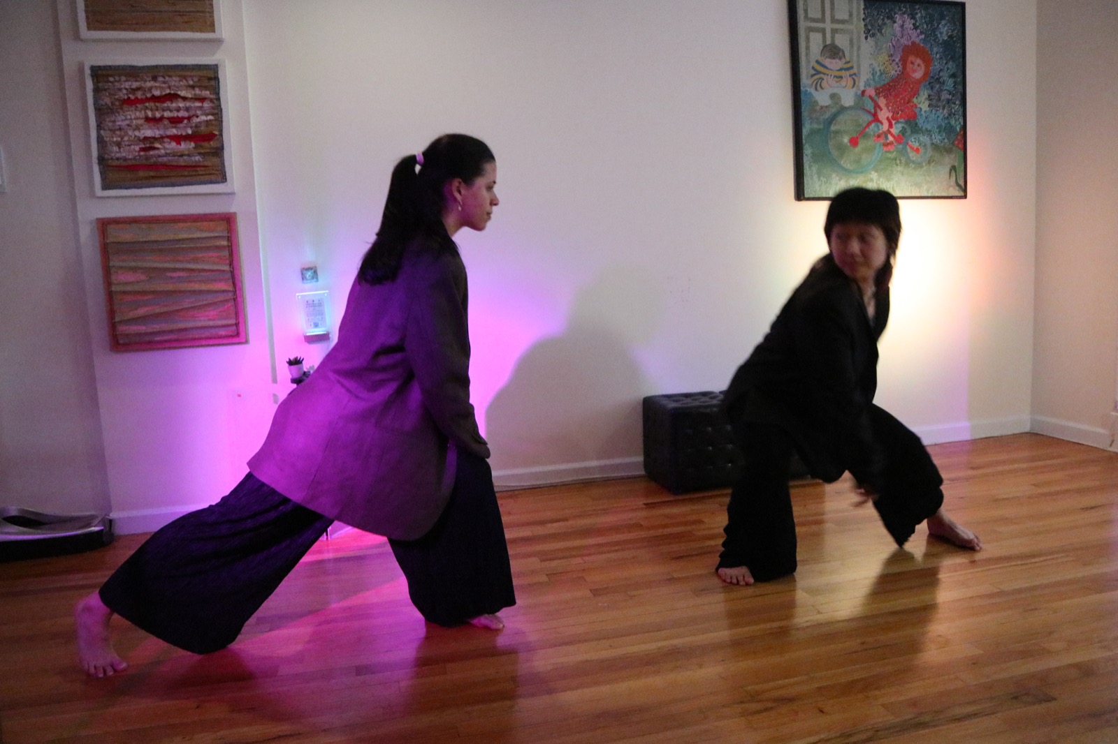 Two dancers in full motion — magenta light, wood floor, the room as collaborator